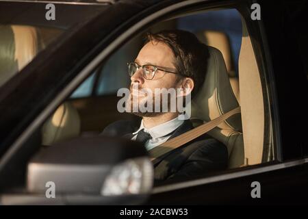 Jeune conducteur portant des lunettes pour regarder la route pendant le trajet dans la voiture Banque D'Images