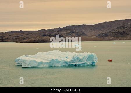 Un petit bateau à côté d'un iceberg dans Krossfjorden, au large de la côte ouest du Spitzberg, dans la lumière du soir. Banque D'Images