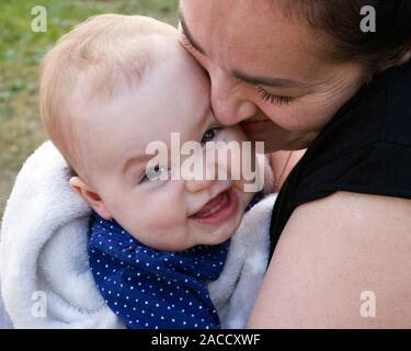 Adorable bébé fille souriante dans les bras de sa mère heureuse Banque D'Images