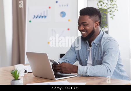 Smiling young businessman using smartphone et working on laptop in office Banque D'Images