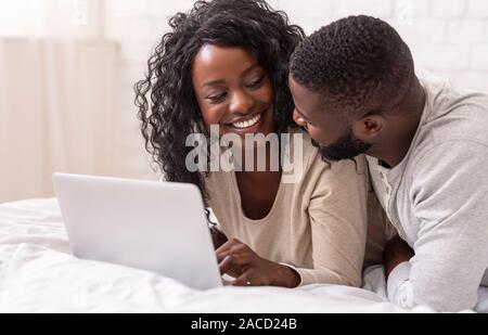 Smiling young couple using laptop in bed at home Banque D'Images