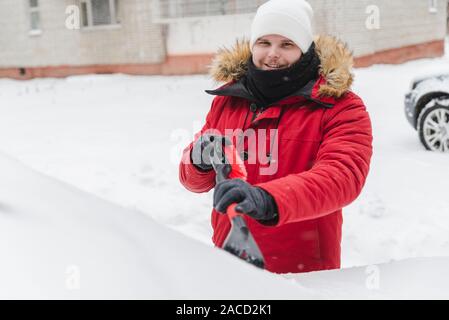 L'homme en rouge avec capuche fourrure manteau d'hiver voiture nettoyage après la tempête de neige Banque D'Images