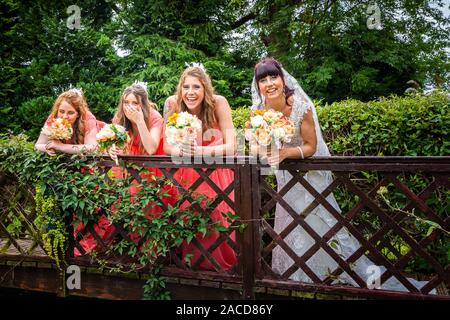 Une magnifique mariée et ses femmes de soudoises se tenant sur un pont orné riant, souriant tout en ayant des photos de mariage prises à l'hôtel Manor à Cheadle Banque D'Images