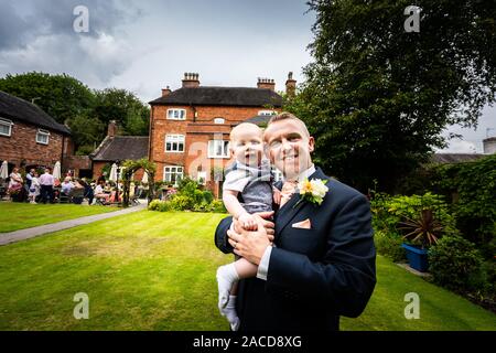 Un marié, père pose avec son bébé garçon après s'être marié dans les jardins du manoir, hôtel, B & B à Cheadle, Stoke on Trent, Staffordshire, jour du mariage Banque D'Images