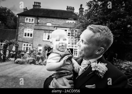 Un marié, père pose avec son bébé garçon après s'être marié dans les jardins du manoir, hôtel, B & B à Cheadle, Stoke on Trent, Staffordshire, jour du mariage Banque D'Images