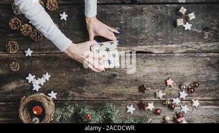 Vue de dessus de la fermeture d'une main de femme holiday gift box avec étoiles d'or au milieu d'un bureau en bois rustique décoré avec des ornements de Noël et decora Banque D'Images
