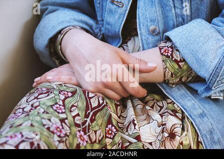 Mid section of young woman wearing denim veste sur robe d'été avec motif floral - Portrait de femme les mains croisées sur ses genoux Banque D'Images