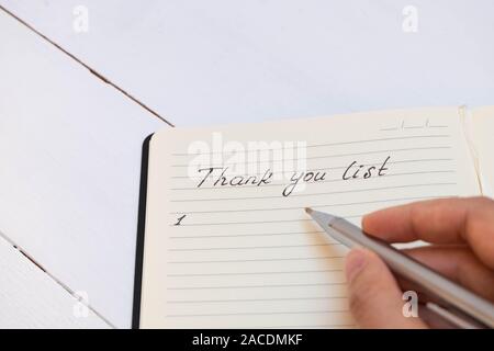 Main femme écrit merci liste dans un journal de gratitude sur table en bois blanc Banque D'Images