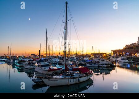 Le ciel jaune se tournant en bleu après le coucher du soleil à Ramsgate Harbour, dans le Kent, en Angleterre. Premier plan, petits bateaux et yachts, beaucoup illuminés avec des lumières de Noël, dans la marina dans le port intérieur, et à travers les nombreux mâts de yachts, un groupe de ciel jaune et orange après le coucher du soleil. Banque D'Images