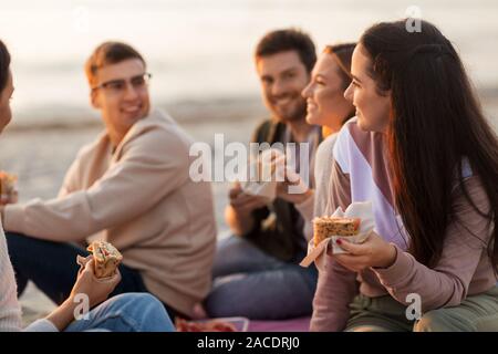 Happy friends eating sandwiches au picnic on beach Banque D'Images