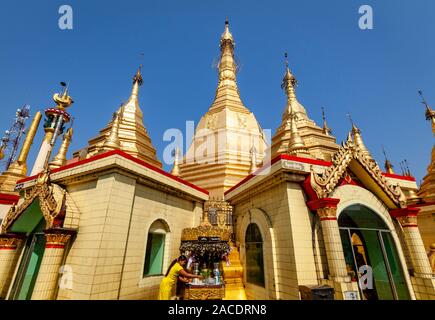 Une jeune femme versant une tasse d'eau sur une petite statue de Bouddha, la pagode Sule, Yangon, Myanmar. Banque D'Images