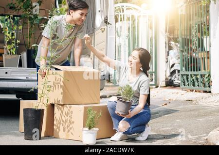 Jolie jeune femme vietnamienne contrôler les feuilles des plantes après son transport dans nouvelle maison Banque D'Images