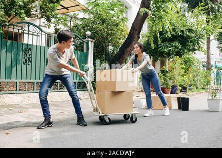 Jeune couple vietnamien à l'aide de panier chariot lors du déplacement dans la nouvelle maison et le transport des boîtes de carton et des plantes Banque D'Images