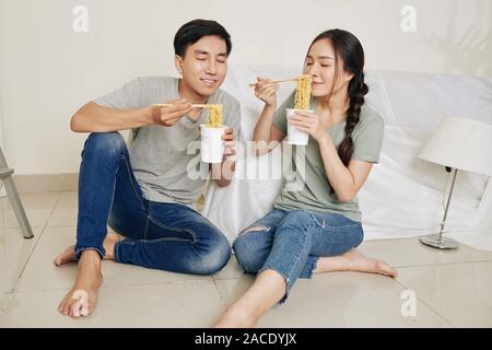 Les jeunes qui ont faim Asian couple appréciant l'odeur de nouilles instantanées qu'ils ont pour le déjeuner après déménagement dans appartement neuf Banque D'Images