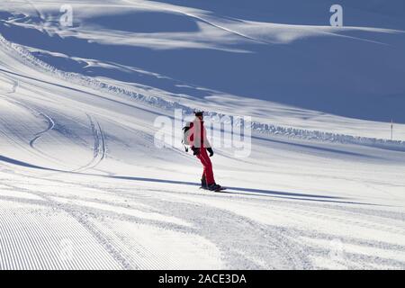 Snowboarder en rouge en descente sur une piste de ski éclairée par snowy préparé par le toilettage la machine à la soirée d'hiver ensoleillé Banque D'Images