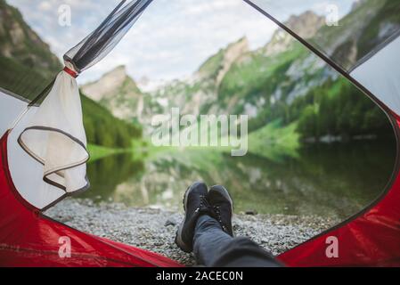 Les pieds de la femme sortent de la tente par le lac Seealpsee dans les Alpes d'Appenzell, en Suisse Banque D'Images