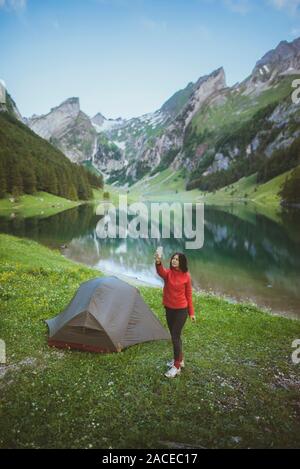 Femme prenant une photo en tente près du lac Seealpsee dans les Alpes d'Appenzell, en Suisse Banque D'Images