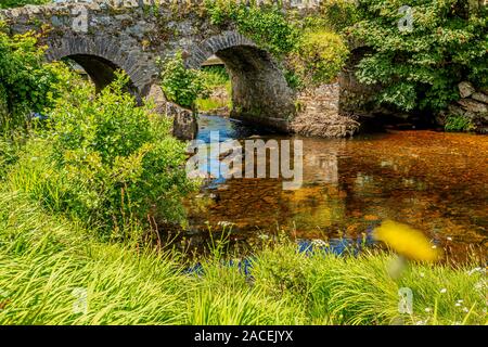 Vieux Pont sur l'Ardbear Owenglin ou rivière Owenglen avec de l'eau transparente et entourée de végétation verte, ensoleillée et journée calme à Clifden Banque D'Images