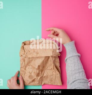 La tenue d'une main de femme deux sac en papier pour l'emballage des produits alimentaires avec les taches graisseuses sur un fond rose vert, concept de rejet de sacs en plastique aux Banque D'Images