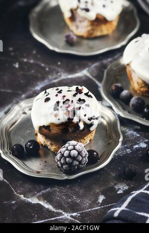De délicieux muffins aux bleuets avec glaçage au chocolat blanc décorée sur les plateaux d'étain aux fruits rouges sur fond de marbre noir Banque D'Images
