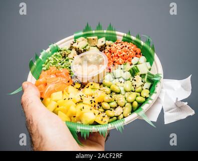 Tenir la main de l'homme contre l'arrière-plan gris Poke bol avec bio frais salade japonaise Banque D'Images