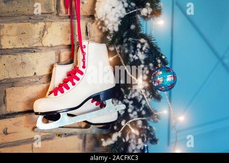 Paire de patins en cuir vintage blanc avec lacets rouge pendaison le vieux mur de brique rustique avec guirlande phares sur décoration d'arbre de Noël. Scenic confortable Banque D'Images