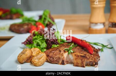 Griller des steaks. Plat de viande sur une plaque d'ajouter aux champignons, salade et poivron rouge Banque D'Images