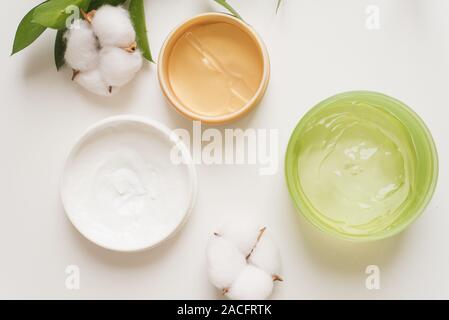 Pots de crème, gel d'aloès et de patchs hydratant visage sur un fond blanc à côté des fleurs de coton. La nature des produits de beauté et soins de la peau du visage à la main, un moi Banque D'Images