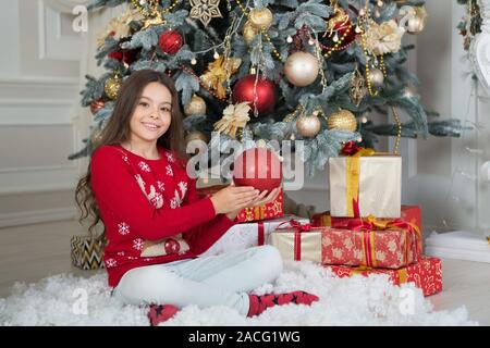 Mes vacances d'hiver parfait. Petite fille près de l'arbre de Noël. Enfant célébrer Noël à la maison. Traditions d'hiver. Boutique cadeaux concept. Porter le chandail de Noël pour enfants adorables. Décor d'attributs de Noël. Banque D'Images