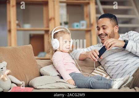 Portrait of cute little girl wearing gros écouteurs et écouter de la musique avec papa à la maison, copy space Banque D'Images