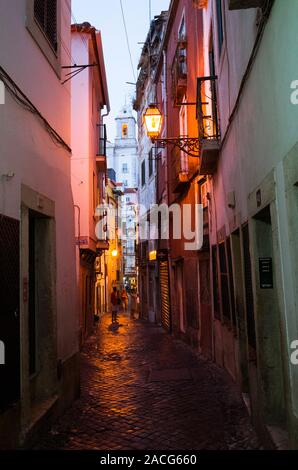 Lisbonne, Portugal : la nuit tombe sur une ruelle pittoresque de l'Alfama, le plus vieux quartier de Lisbonne. Santo Estevao clocher en arrière-plan. Banque D'Images