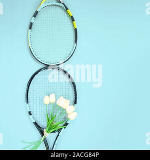 Journée internationale de la femme le 8 mars en forme de raquettes avec bouquet de tulipes blanches et de copier l'espace sur fond bleu pastel. Valentine's day concept avec tennis. Mise à plat, vue du dessus. Banque D'Images