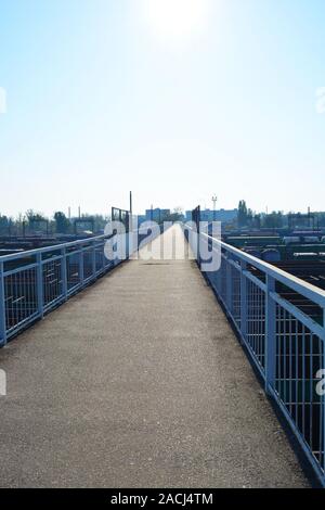 Un étroit pont en béton armé gris sur une jonction de chemins de fer et les trains de marchandises éclairées par le soleil avec ciel bleu. Banque D'Images