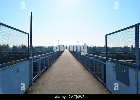 Un étroit pont en béton armé gris sur une jonction de chemins de fer et les trains de marchandises éclairées par le soleil avec ciel bleu. Banque D'Images