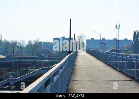 Un noir corbeau solitaire est assis sur la rambarde d'un pont en béton armé gris sur une jonction de chemins de fer et les trains de marchandises éclairées par un soleil éclatant. Banque D'Images