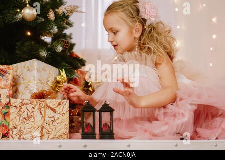 Jeune fille dans une robe rose près de l'arbre de Noël et des boîtes à cadeaux Banque D'Images