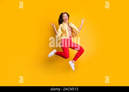 La taille du corps tourné sur toute la longueur de la photo montrant une femme criant joyeux doigts cornu signe rock pantalon rouge en portant des chaussures de couleur vive isolé blanc Banque D'Images