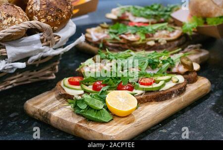 Des sandwichs avec tomates, laitue, jambon, roquette et citron sur du pain noir. Banque D'Images