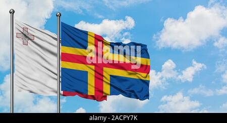 Malte et les îles Aland drapeaux dans le vent contre ciel bleu nuageux blanc ensemble. Concept de diplomatie, de relations internationales. Banque D'Images