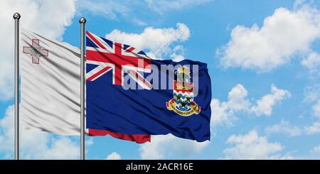 Malte et les Îles Caïmanes drapeaux dans le vent contre ciel bleu nuageux blanc ensemble. Concept de diplomatie, de relations internationales. Banque D'Images