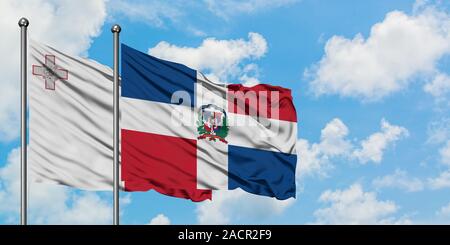 Malte et de brandir le drapeau de la République dominicaine dans le vent contre ciel bleu nuageux blanc ensemble. Concept de diplomatie, de relations internationales. Banque D'Images