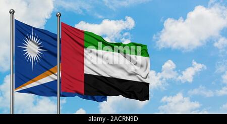 Îles Marshall et Emirats Arabes Unis drapeaux dans le vent contre ciel bleu nuageux blanc ensemble. Concept de diplomatie, de relations internationales. Banque D'Images