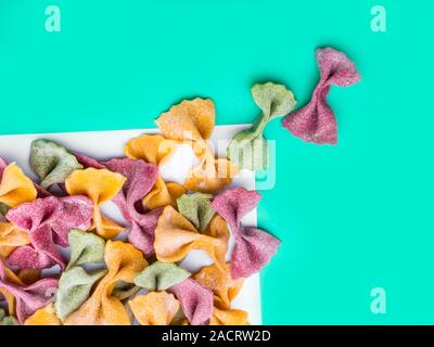 Pile de couleur Tri séchées italiennes pâtes farfalle. Différentes couleurs de nœud papillon sur fond couleur menthe verte à la mode Banque D'Images