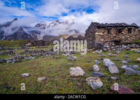 Vieille maison en pierre sur un pré en dessous du col Renjo La, paysage montagneux, couvert de nuages de mousson dans la distance Banque D'Images