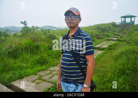 Un homme portant une casquette, lunettes et T- shirt posant pour une photo dans le parc de l'Eco avec le pavillon, Haïfa Gazebo dans l'arrière-plan. Banque D'Images