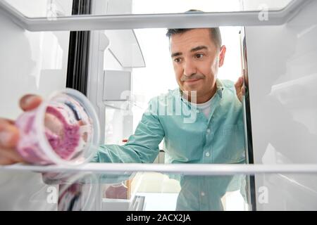 Alimentation et régime alimentaire concept - homme d'âge moyen en tenant le récipient avec de la nourriture, des restes de cuisine réfrigérateur à Banque D'Images