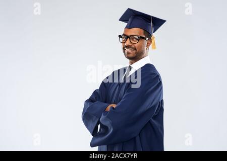 L'éducation, l'obtention du diplôme et les gens concept - happy smiling Indian male étudiant diplômé en administration et du baccalauréat de mortier sur fond gris robe Banque D'Images