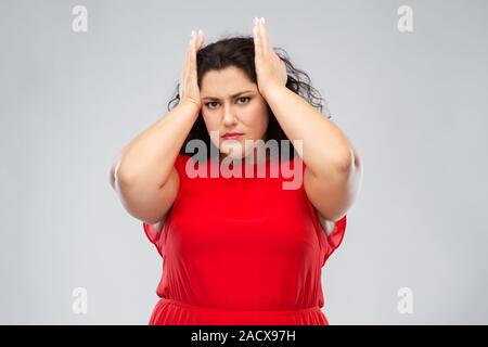 Les gens et portrait concept - femme en robe rouge qui souffrent de maux de tête sur fond gris Banque D'Images