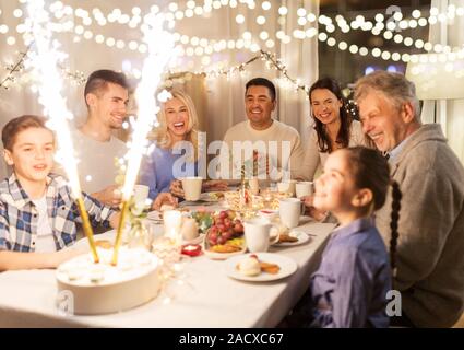 Fête, anniversaire et personnes concept - happy family dinner party avec fontaine d'artifice ou sparkler bougies sur cake at home Banque D'Images