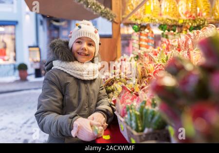 Jours fériés, de l'enfance et de personnes concept - happy little girl le choix des bonbons au marché de noël en soirée d'hiver Banque D'Images